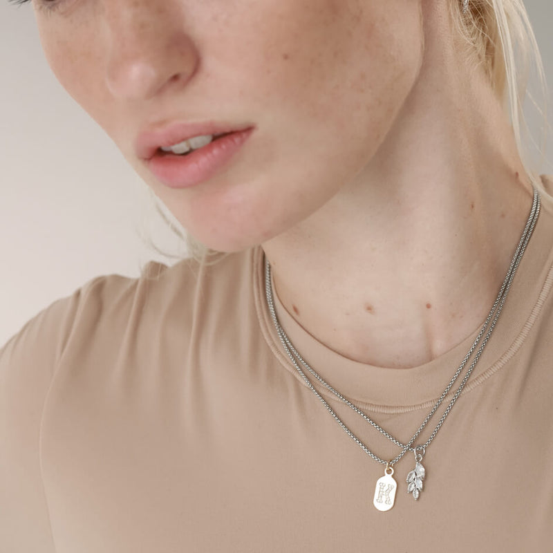 Model wearing the LETTER DAINTY NECKLACE made of Stainless steel chain 1mm wide chain and Gold filled encrusted zirconia initials charm and another necklace with similar chain and  5 leaf shaped crystal charm. 