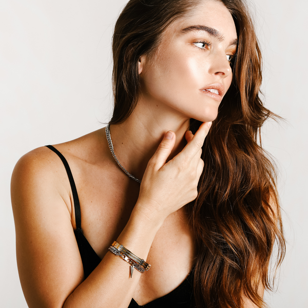 Model wearing a silver chain necklace and the Iron stack which comes with two bracelets. One is the Iron Bracelet which is a 7 inches Stainless steel chain with two gold plated triangle charms and the Marinero Bangle which is a Stainless steel 18K gold plated bangle with silver details.