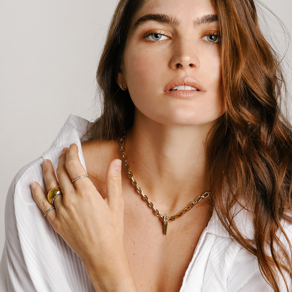 Model wearing the bamboo necklace which is a 17 inches Gold chain necklace with 5 Triangle charms & Zirconia stacked together into a one charm.  She is also wearing three rings on her right hand and small hoop earrings.
