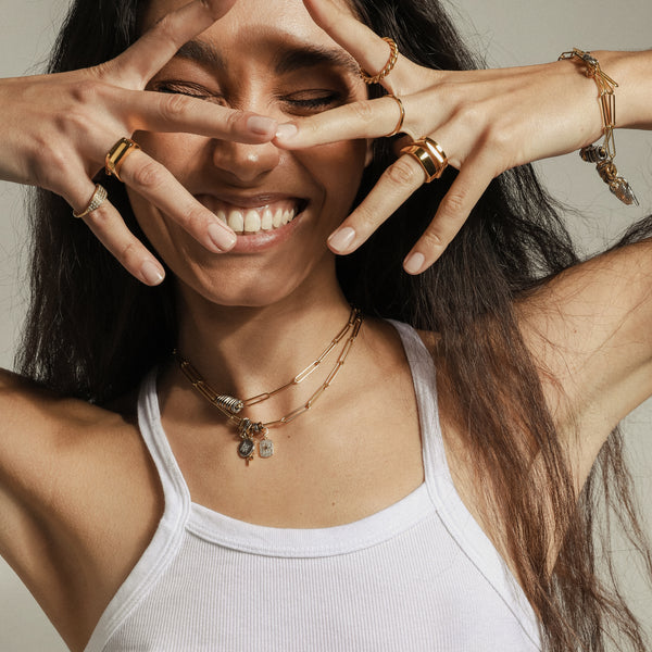 Model wearing the ZIRCONIA DOTS RING which is an 18k Gold plated thin ring with encrusted cubic zirconia. She is also wearing the Shape stack ring and also the link charm bracelets and necklaces.