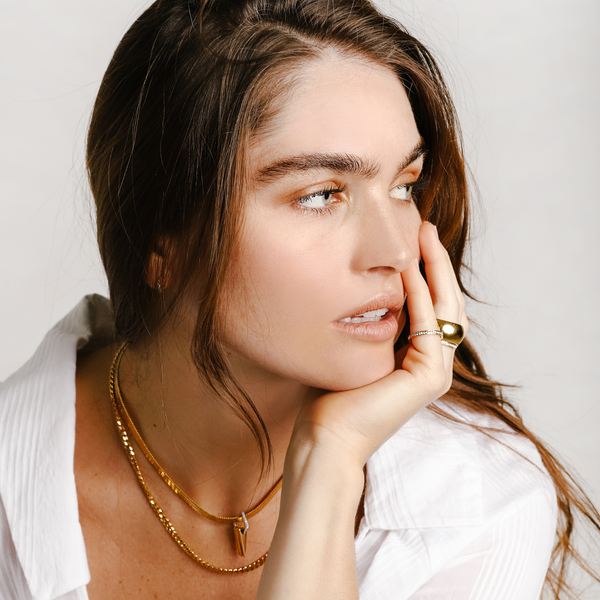 Model wearing the VIENTOS LAYERED NECKLACE SET which includes 2 separate chains. One is a 16 inches Stainless steel 18k gold plated snake necklace with Triangle charms & Zirconia and 20 inches gold plated chain necklace. She is also wearing the orbit ring and seeds ring both in gold.