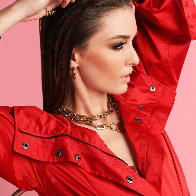 Model in red jacket wearing the PUERTO LOCK NECKLACE which has a chain made of mix silver and gold links and Stainless steel 18k gold plated lock pendant.