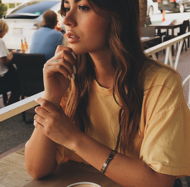 Model sitting in a restaurant wearing the Marinero bangle in gold with silver details.