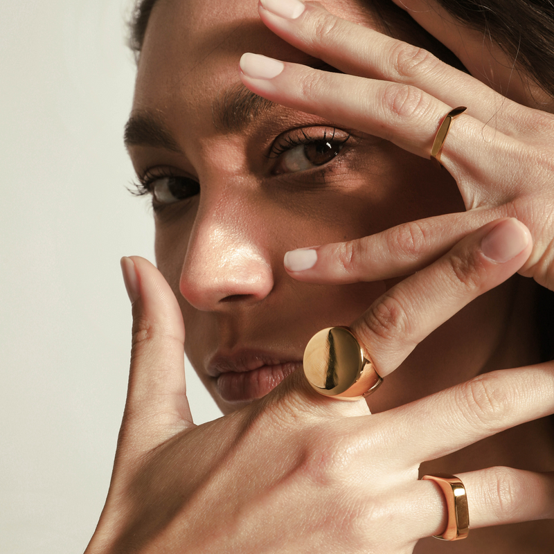 Model wearing The SOLO GOLD RING which is made of an 18k Gold plated Stainless steel. It's an oversized flat oval shaped ring. She is also wearing the rhombus and the rectangle rings. 