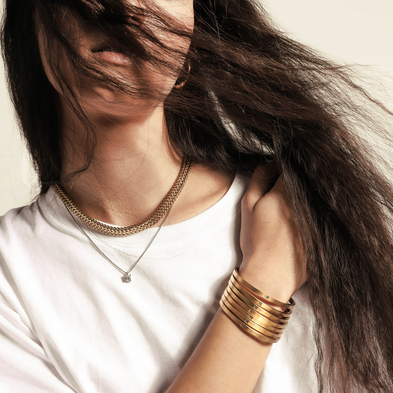 Model wearing a stack of ONE BANGLES which is made of 18k gold plated Stainless steel bangle with one encrusted zirconia in the middle. She is also wearing the  Marinero Layered Necklace set.
