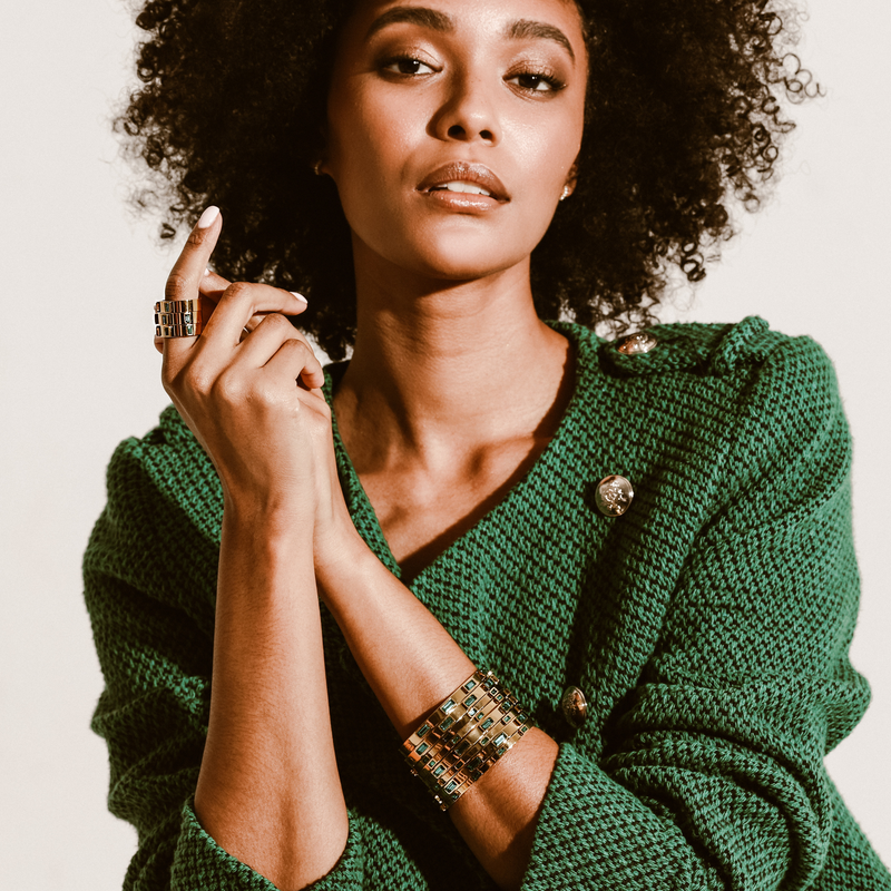 Model wearing a stack of Emerald Bangle and Emerald thin bangles. She is wearing three emerald rings that are gold plated stainless steel with three emerald stones encrusted. 