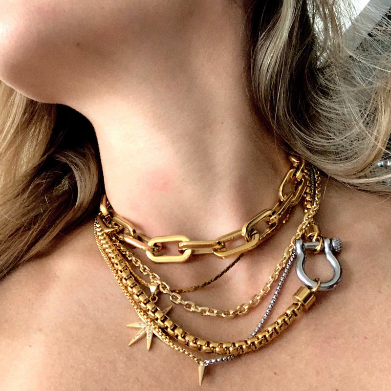Model wearing the Herradura Mix Necklace in silver chain and gold clasp. It is layered with other necklaces like gold big chains worn tightly to the neck, thin gold necklace and half golf half silver necklace with spike pendant.