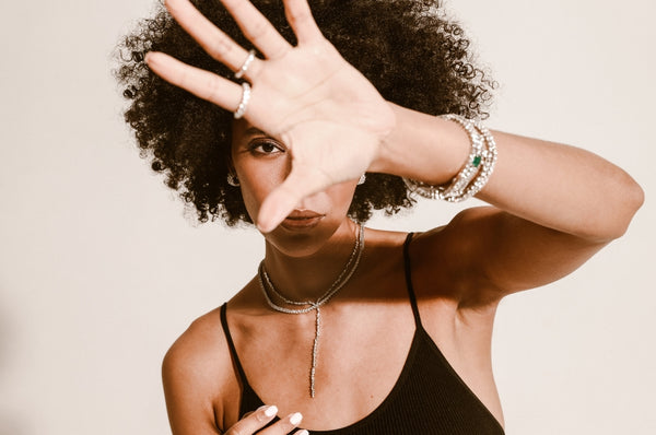 Woman posing to the camera with her hand infront wearing various Artizan rings, tennis bracelets and necklaces