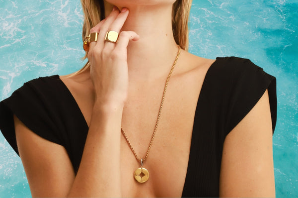 Woman showing Artizan Yellow Gold Rings and Necklace with a water background