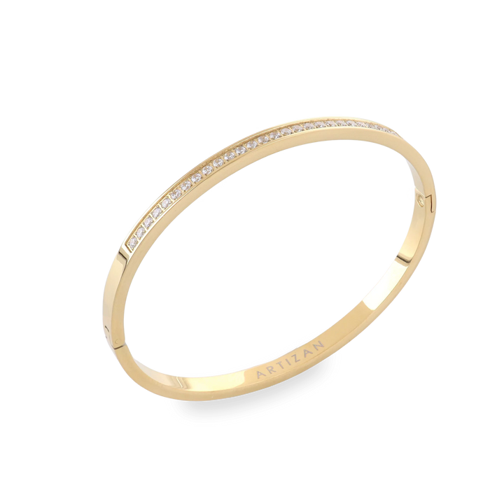 The DUST BANGLE, which is a single gold bracelet, features a sleek and minimalistic design adorned with a row of sparkling stones for an added touch of elegance. This timeless piece is perfect for layering or wearing solo, offering a refined and versatile look. ||| GOLD