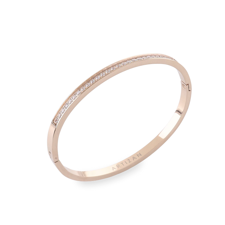 The DUST BANGLE, which is a single rose gold bracelet, features a sleek and elegant design adorned with a delicate row of shimmering stones along its band. This sophisticated piece adds a subtle sparkle, perfect for stacking or wearing solo for a refined touch. ||| ROSE GOLD
