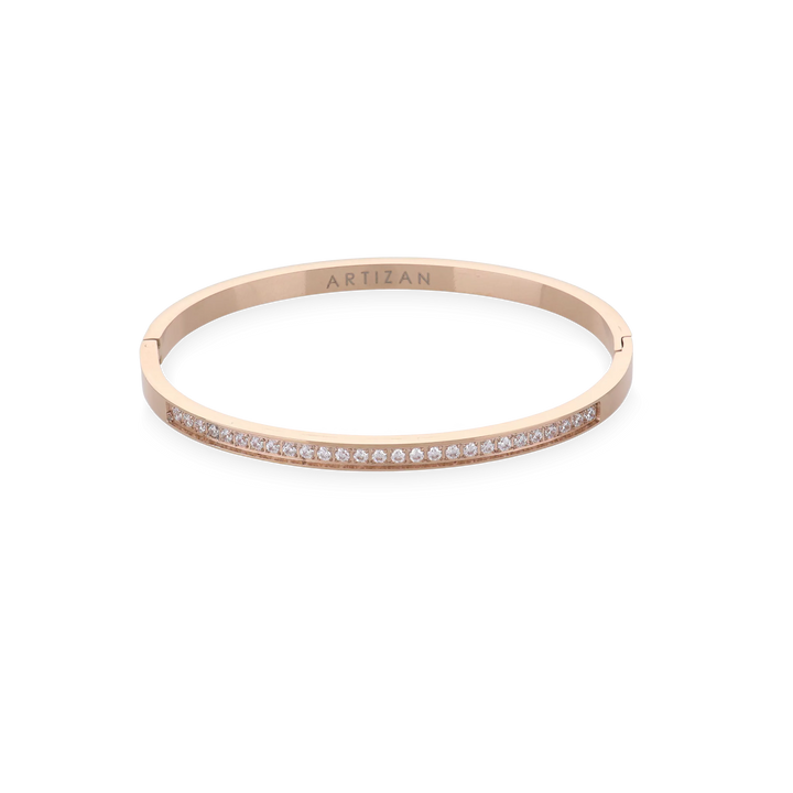 The DUST BANGLE, which is a single rose gold bracelet, features a sleek and elegant design adorned with a delicate row of shimmering stones along its band. This sophisticated piece adds a subtle sparkle, perfect for stacking or wearing solo for a refined touch. ||| ROSE GOLD