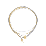 The Letter Necklace Set, which is a three-piece layered necklace set, features a combination of gold and silver chains with two unique charms—a square charm engraved with a letter 'X' and a small lightning bolt pendant.