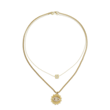 The I See You Necklace, a layered gold necklace featuring two chains. The shorter chain has a dainty square charm with an initial, while the longer chain showcases a striking sunburst pendant with an eye design encrusted in crystals. This mystical-inspired piece adds depth and personality, perfect for layering with other gold accessories or wearing solo for a bold look.