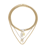 The Just Click Tag Necklace Set, a four-piece gold necklace set featuring a Cuban link chain, a box chain, and a rope chain with diamond-like accents, two dog tag charms, and a spike charm.