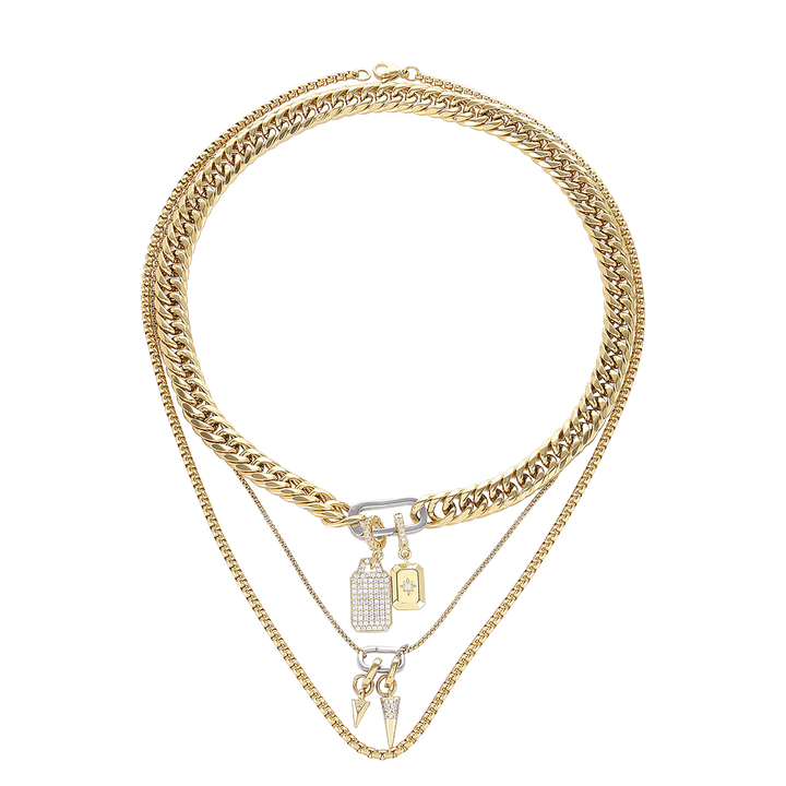 The Just Click Tag Necklace Set, a four-piece gold necklace set featuring a Cuban link chain, a box chain, and a rope chain with diamond-like accents, two dog tag charms, and a spike charm.