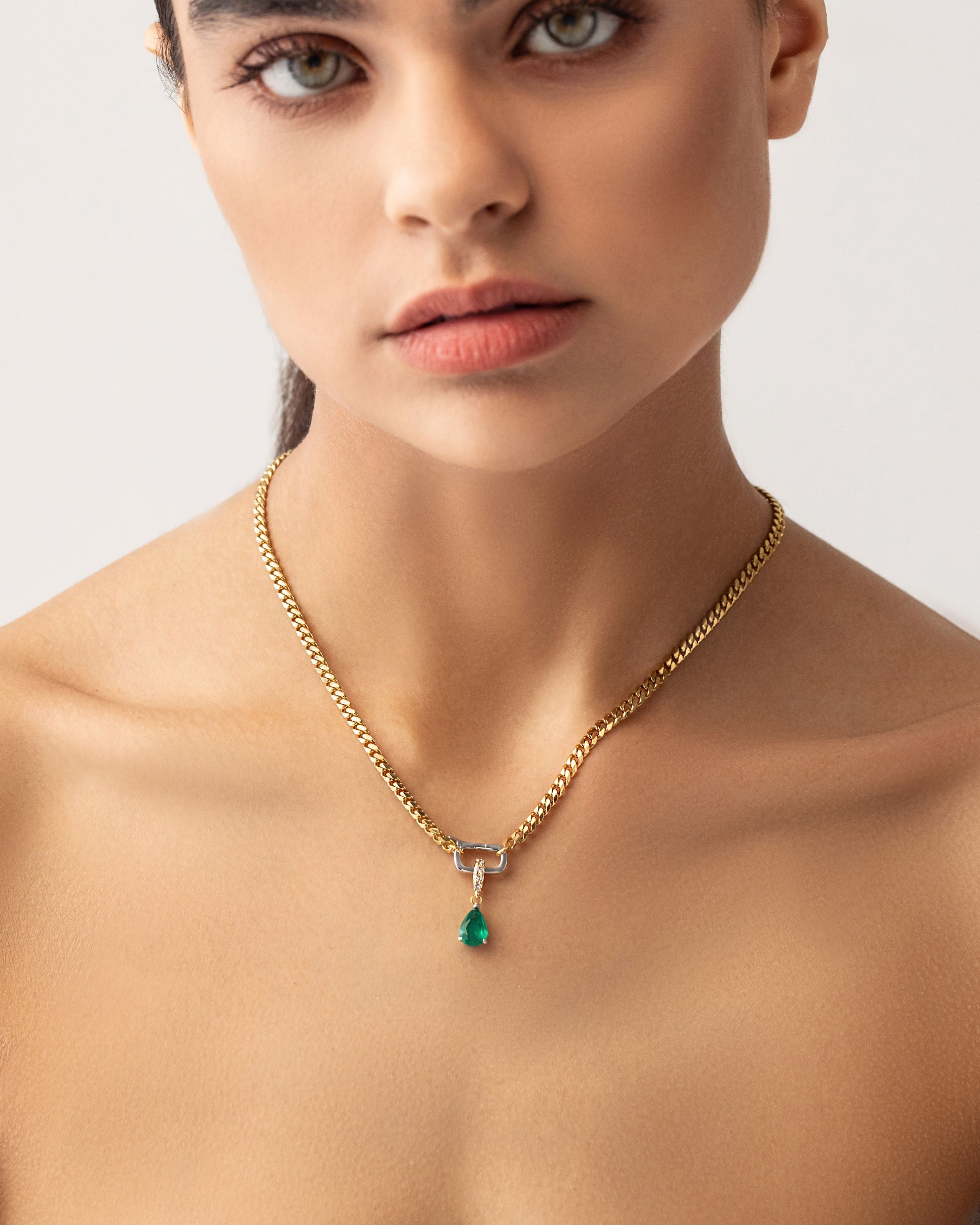 Model wearing a gold necklace with can opener clasp with the Emerald Teardrop Clip On Charm, a gold charm featuring a single teardrop-shaped emerald.  ||| SILVER