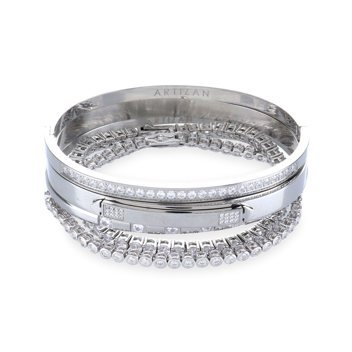 The Silver Gear Bracelet Stack, a five piece silver bracelet stack includes three unique bangle styles, one featuring a row of sparkling stones and another with a sleek, minimalist design. Two delicate tennis bracelets with shimmering stones.
