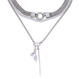 The Needle and The Tennis, which is a layered silver necklace stack, features a combination of a sleek needle pendant and a sparkling tennis chain adorned with crystals. This elegant set includes multiple silver chains with detailed charms, creating a bold yet sophisticated statement piece