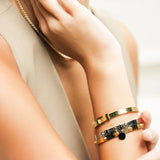 Model wearing the BALANCE BRACELET STACK, a stylish three-piece bangle set featuring a mix of gold and silver tones with intricate details like a buckle clasp and studded accents. Perfect for adding a touch of edgy elegance to any outfit.