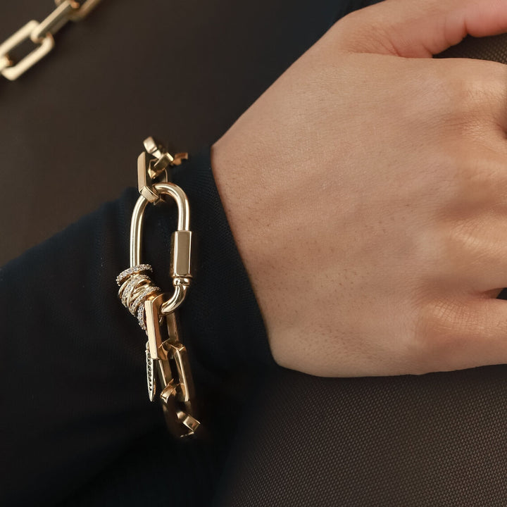 Model wearing the Carabiner Square Spiga Bracelet, a gold chain bracelet featuring a square spiga chain and a carabiner clasp with diamond accents and spike charm with stones.