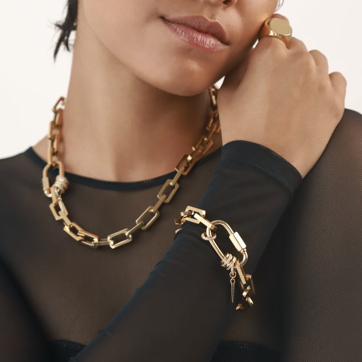 Model wearing the The Carabiner Square Spiga Bracelet and necklace, a gold chain bracelet featuring a square spiga chain and a carabiner clasp with diamond accents and spike charm with stones. 