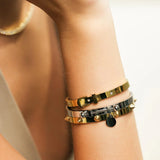 Model wearing the BALANCE BRACELET STACK, a stylish three-piece bangle set featuring a mix of gold and silver tones with intricate details like a buckle clasp and studded accents. Perfect for adding a touch of edgy elegance to any outfit.
