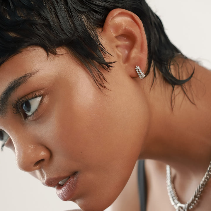 The Leaf Crystal Huggies, which are delicate silver huggie earrings, feature a graceful leaf-inspired design adorned with multiple sparkling crystals. These earrings sit snugly on the ear, offering a refined and nature-inspired elegance ideal for both everyday wear and special occasions.