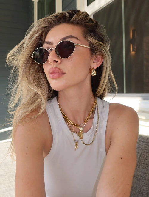 3-piece layered gold necklace set featuring chunky and dainty chains with charm details, worn by a model and paired with bold gold statement hoop earrings.