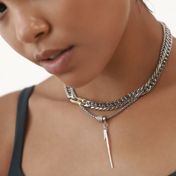 The Needle Necklace, which is a single-piece silver necklace, showcases a bold needle-shaped pendant hanging elegantly from a textured chain, exuding a modern and edgy aesthetic perfect for layering or wearing solo.