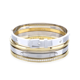 The BELTED BRACELET STACK, a stylish four-piece bangle set featuring a mix of gold and silver tones with intricate details like a buckle clasp and diamond accents. 