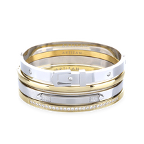 The BELTED BRACELET STACK, a stylish four-piece bangle set featuring a mix of gold and silver tones with intricate details like a buckle clasp and diamond accents. 