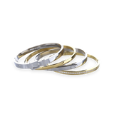 The BELTED BRACELET STACK, a stylish four-piece bangle set featuring a mix of gold and silver tones with intricate details like a buckle clasp and diamond accents. 