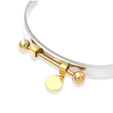 The Coin Bangle is a mixed-metal bracelet featuring a sleek silver band with gold-tone hardware, including a dangling coin charm and bold spherical accents. ||| MIX GOLD