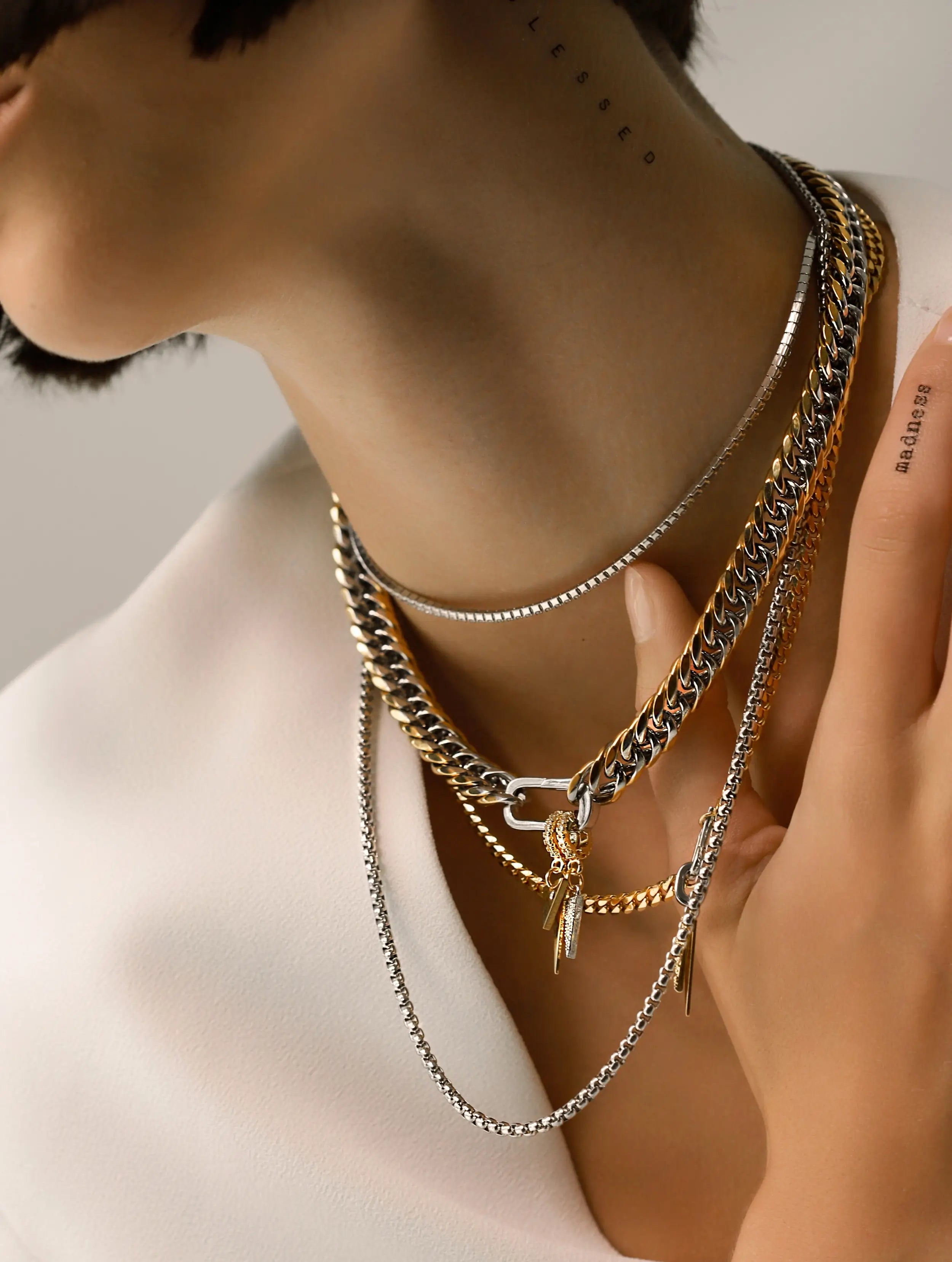 Model wearing a mix of layered chains in gold and silver tones. It includes bold, chunky styles alongside more delicate chains, creating a modern and versatile look. 