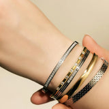 Model wearing the Intense Stack, a five-piece gold and silver bracelet stack featuring bangles with various diamond-like accents and textured designs.