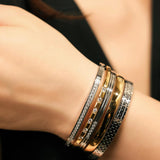 Model wearing the Intense Stack, a five-piece gold and silver bracelet stack featuring bangles with various diamond-like accents and textured designs.