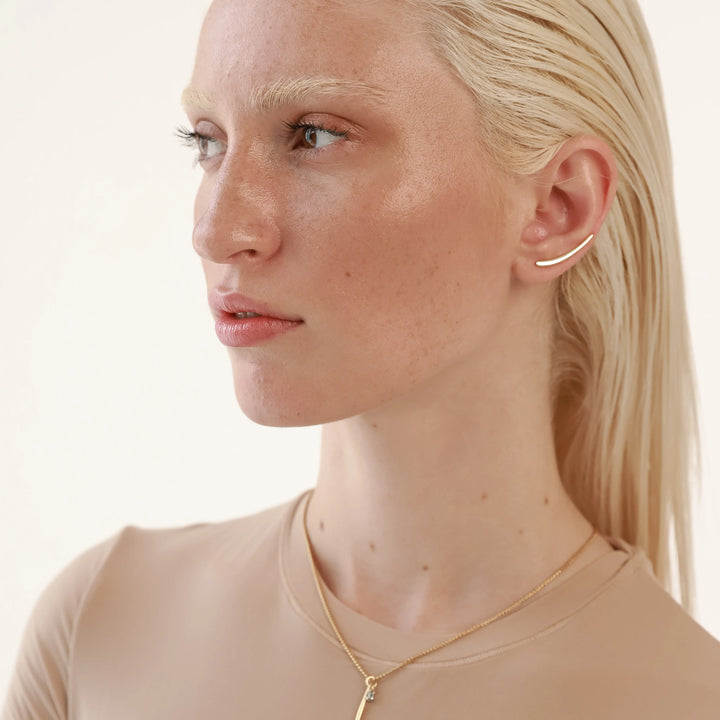 The Line Climber, which is a single-piece gold ear climber earring, features a minimalist curved bar that elegantly follows the contour of the ear for a contemporary and sophisticated look, perfect for adding understated elegance.