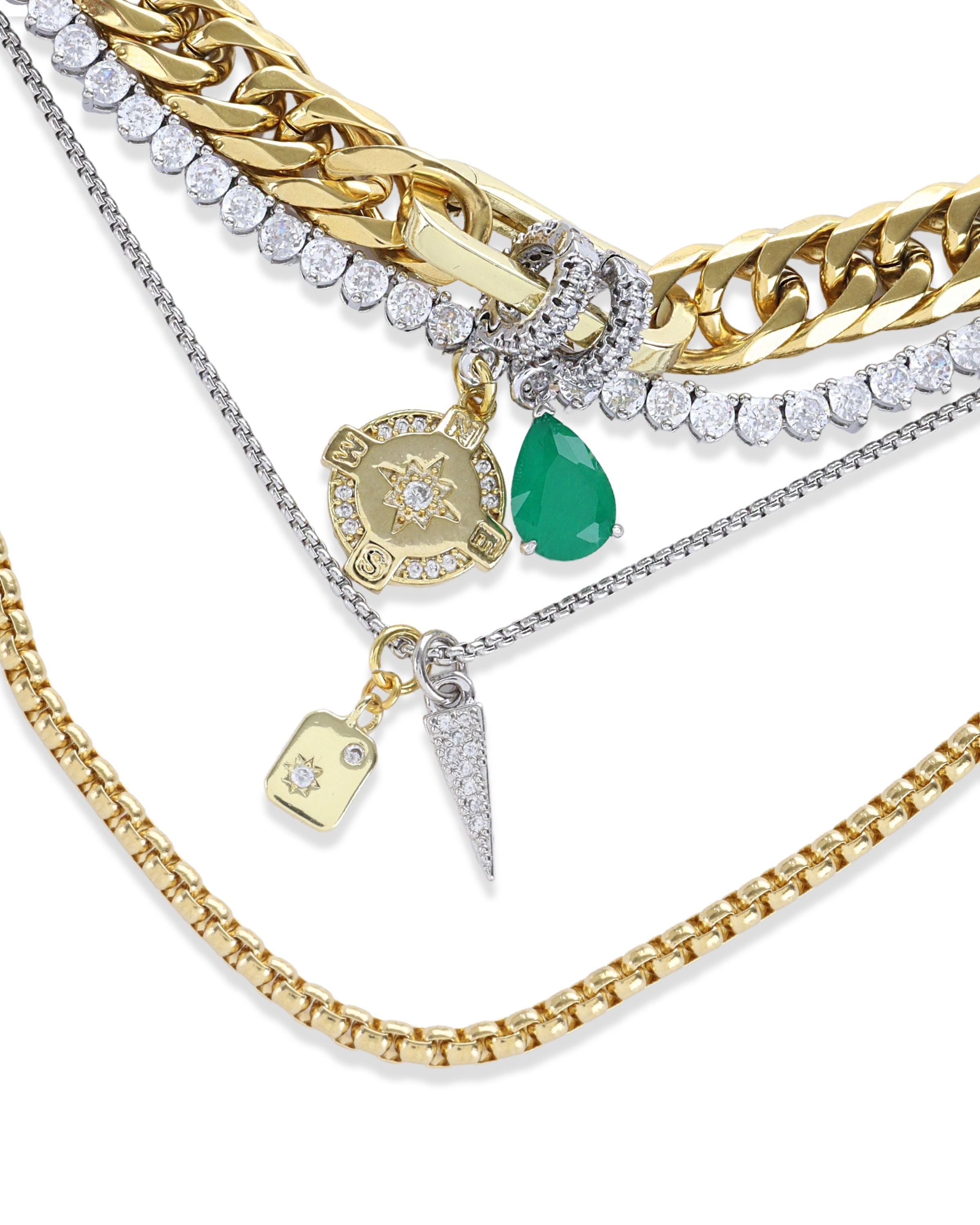 The Just Click Emerald Tennis Necklace Set, a four-piece gold and silver necklace set featuring a variety of chains with diamond-like accents, emerald accents, and a variety of charms.