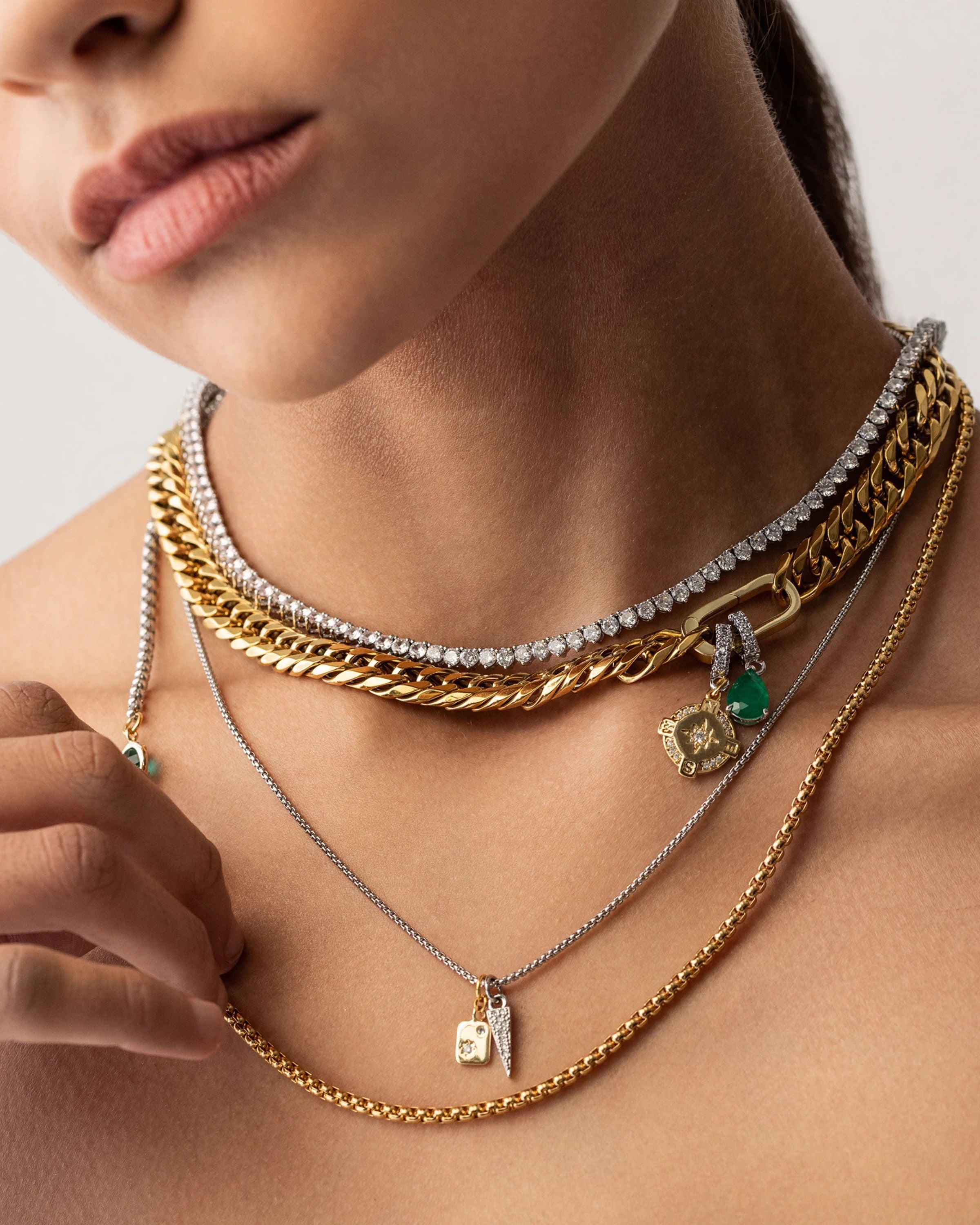 Model wearing the Just Click Emerald Tennis Necklace Set, a four-piece gold and silver necklace set featuring a variety of chains with diamond-like accents, emerald accents, and a variety of charms