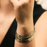 Model wearing the Intense Stack, a five-piece gold and silver bracelet stack featuring bangles with various diamond-like accents and textured designs.