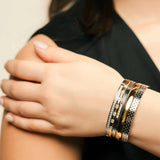 Model wearing the Intense Stack, a five-piece gold and silver bracelet stack featuring bangles with various diamond-like accents and textured designs.