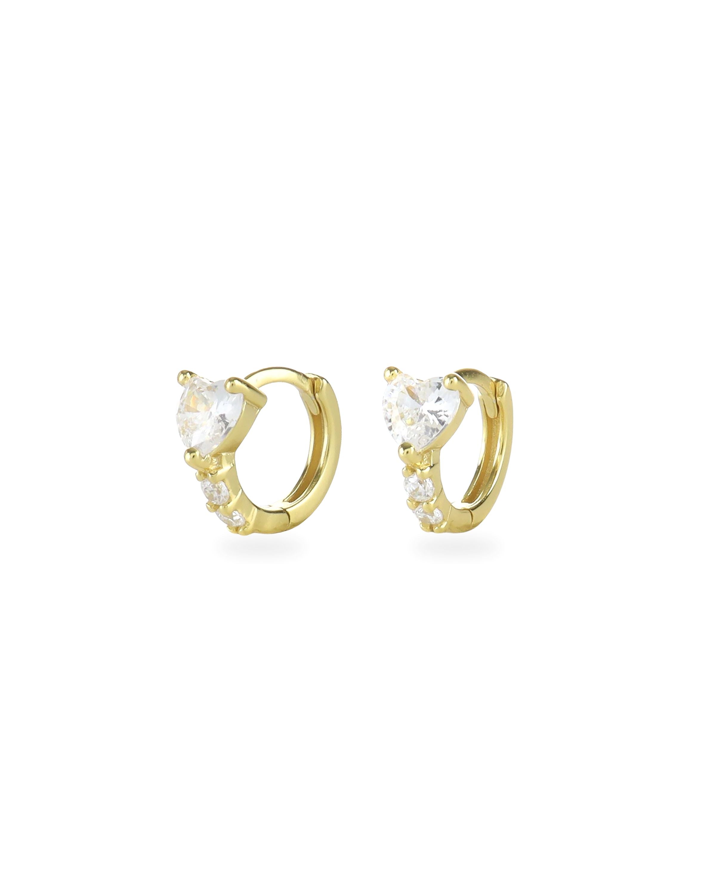 The One Stone Gold Piercing Hoops, which are a pair of gold hoop earrings, feature a central heart-shaped stone with additional sparkling accents along the band.