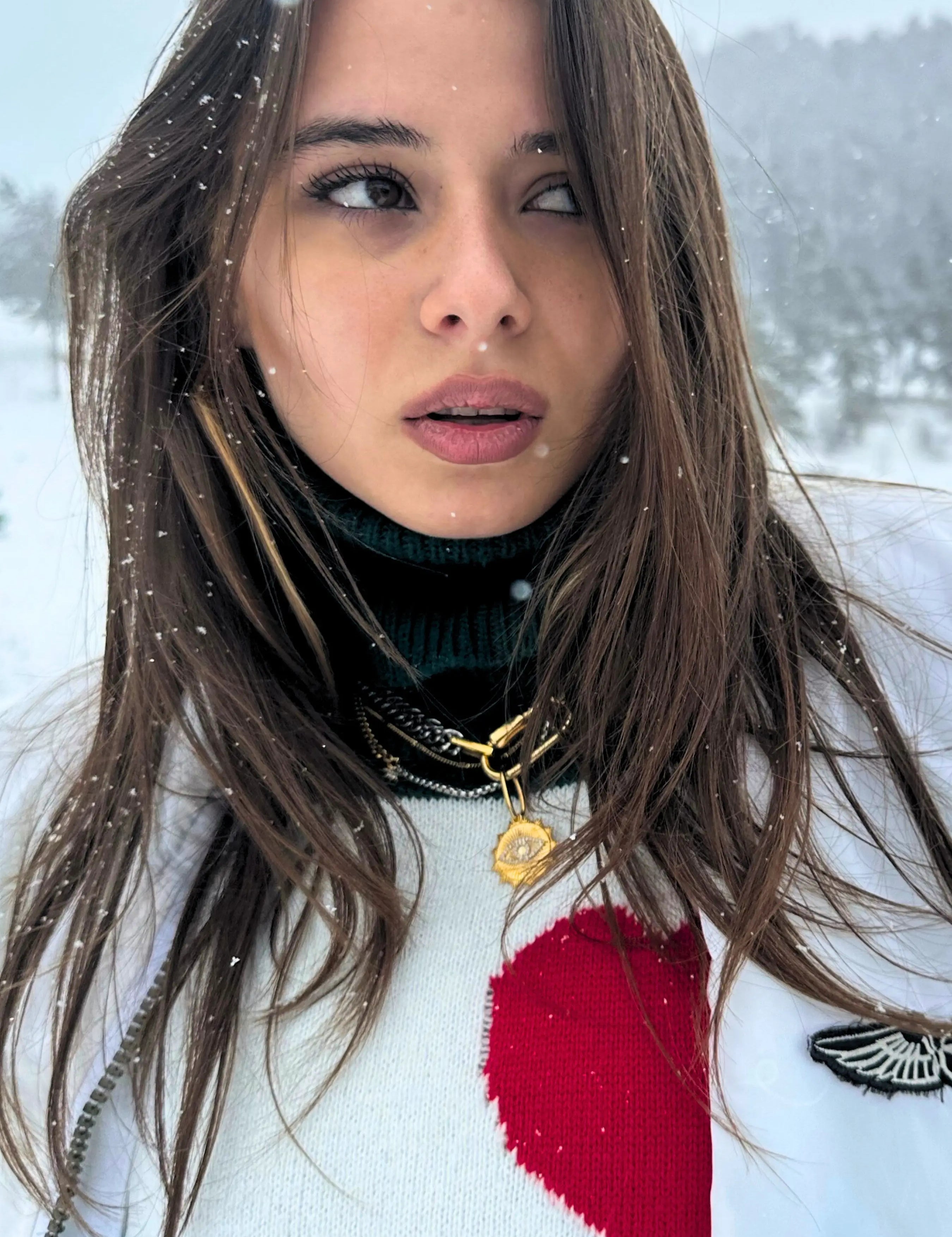 Woman wearing a three-piece layered necklace stack in mixed gold and silver, featuring a gold coin pendant, styled with a winter outfit in the snow.