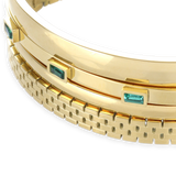 The Queen's Crown Bracelet Stack, a four-piece gold bracelet stack featuring bangles with a variety of accents, including the word "ARTIZAN," emerald accents, and a textured design.