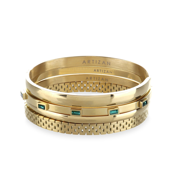 The Queen's Crown Bracelet Stack, a four-piece gold bracelet stack featuring bangles with a variety of accents, including the word "ARTIZAN," emerald accents, and a textured design.
