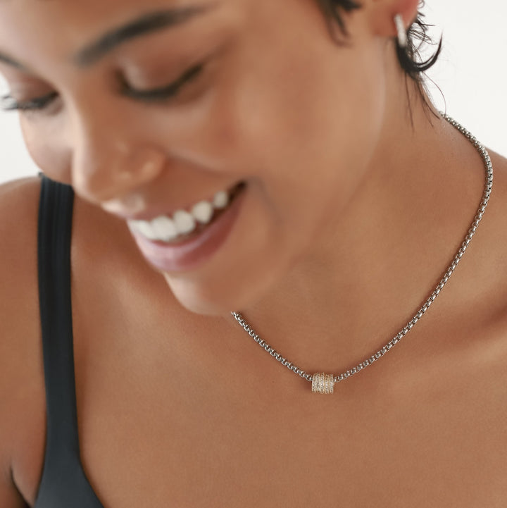 The Nut Necklace, a silver box chain with a gold nut-shaped pendant encrusted with stones, worn by a model. ||| MIX