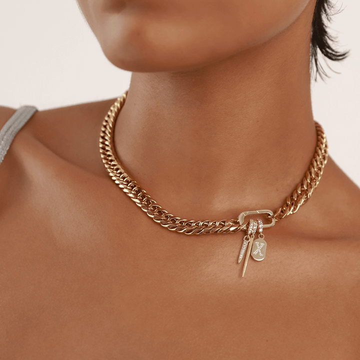 Model wearing the Just Click Letter Chain, a gold chain with a lobster clasp closure and three charms: a diamond-like encrusted letter "X" and two spike charms.