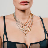 Close-up of woman wearing 5 layered gold and silver necklaces with cross, lightning and celestial charms, styled over a deep green satin top. |||