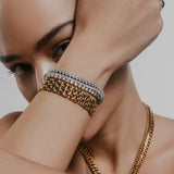 Model wearing a stack of Artizan Joyeria bracelets, featuring a gold chain bracelet and a sparkling diamond-studded bracelet, paired with a bold gold chain necklace.